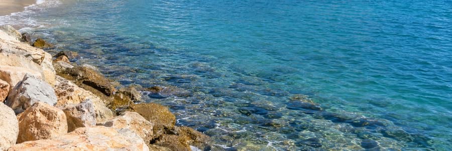 Clear turquoise water lapping over pale rocks at the edge of a sandy beach